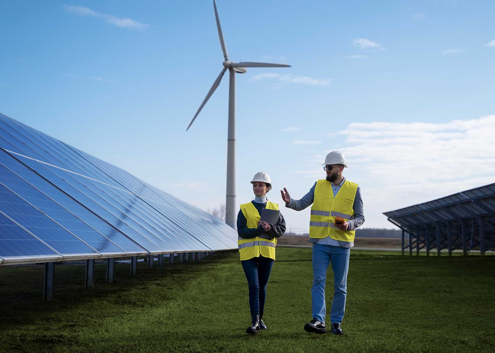 Two engineers in safety vests and helmets standing near a solar farm, reviewing documents on a clipboard, with rows of solar panels and a cloudy sky in the background.