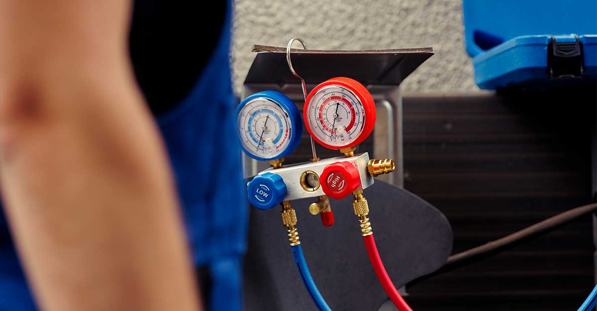 Technician with HVAC manifold gauge set connected by red and blue hoses for measuring and servicing a heat pump or air conditioning system.